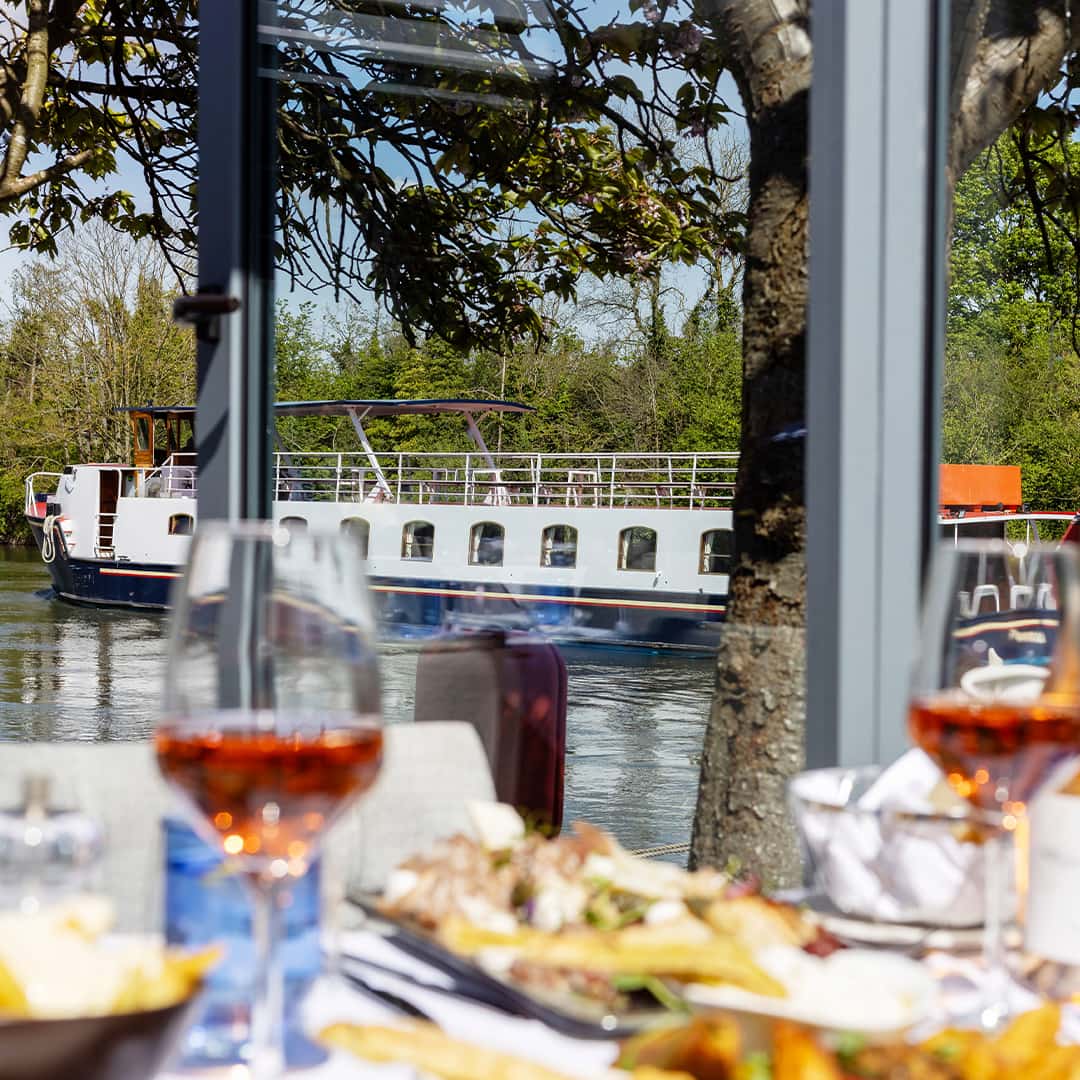A dining table set up at Mediterranevm bray - the background is a passenger boat heading along the River Thames