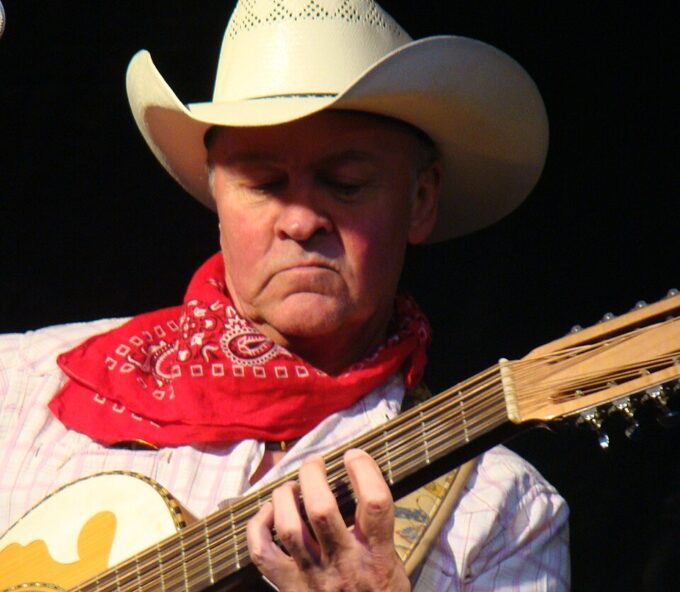A close-up of Paul Young holding a guitar and wearing a hat