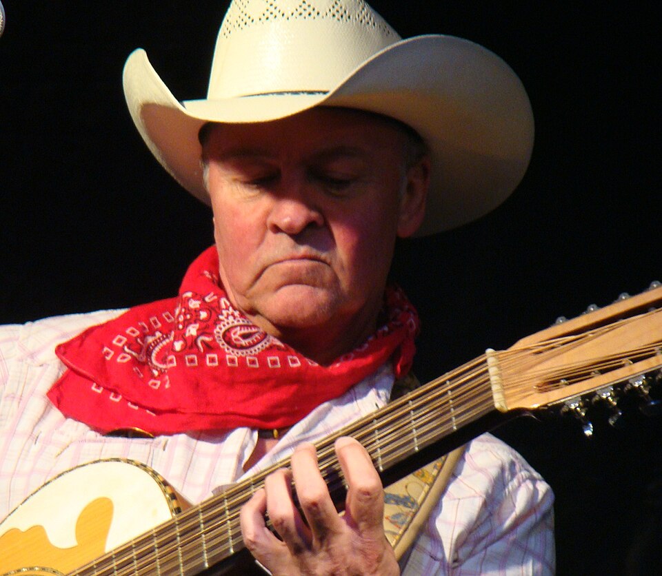 A close-up of Paul Young holding a guitar and wearing a hat