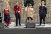 A rehearsal image for Progress Theatre's Hamlet showing four actors in a line on a stage that has been erected in Reading's Abbey Ruins, which can be seen in the background