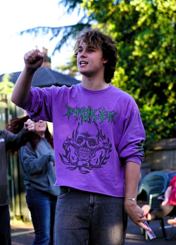 A man in a purple sweatshirt with one arm aloft, the other by his side, cupped