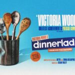 A promotional poster with a light blue background. On the left, a metal catering tin holds five wooden and metal kitchen spoons, each featuring a hand-drawn cartoon face representing a character. To the right, large stylized text reads Victoria Wood’s dinnerladies, along with subtitles stating a brand new stage adaptation, adapted for the stage by Beth and Emma Kilcoyne, and directed by Sean Foley. An orange circle notes the show is produced by the Victoria Wood Estate. A quote from The Telegraph reads, Victoria Wood’s greatest achievement is precise comic gold. A small circular insert in the bottom right features a portrait of a smiling Les Dennis, labelled starring Les Dennis as Stan.
