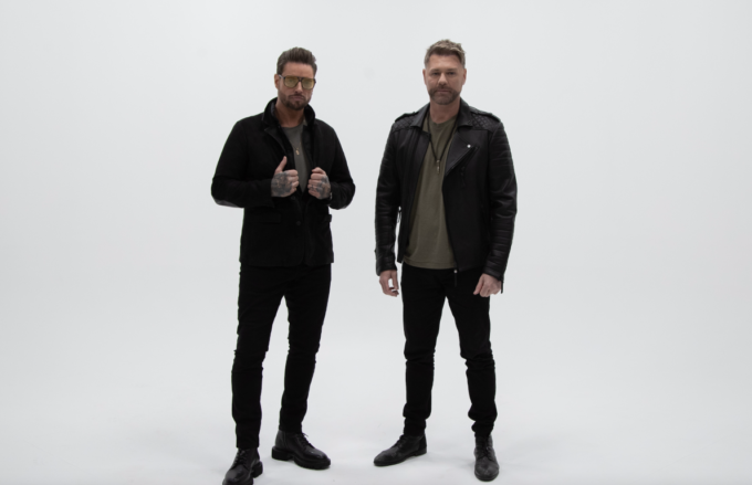 Keith Duffy and Brian McFadden of Boyzlife standing side by side against a white studio background wearing black jackets and trousers