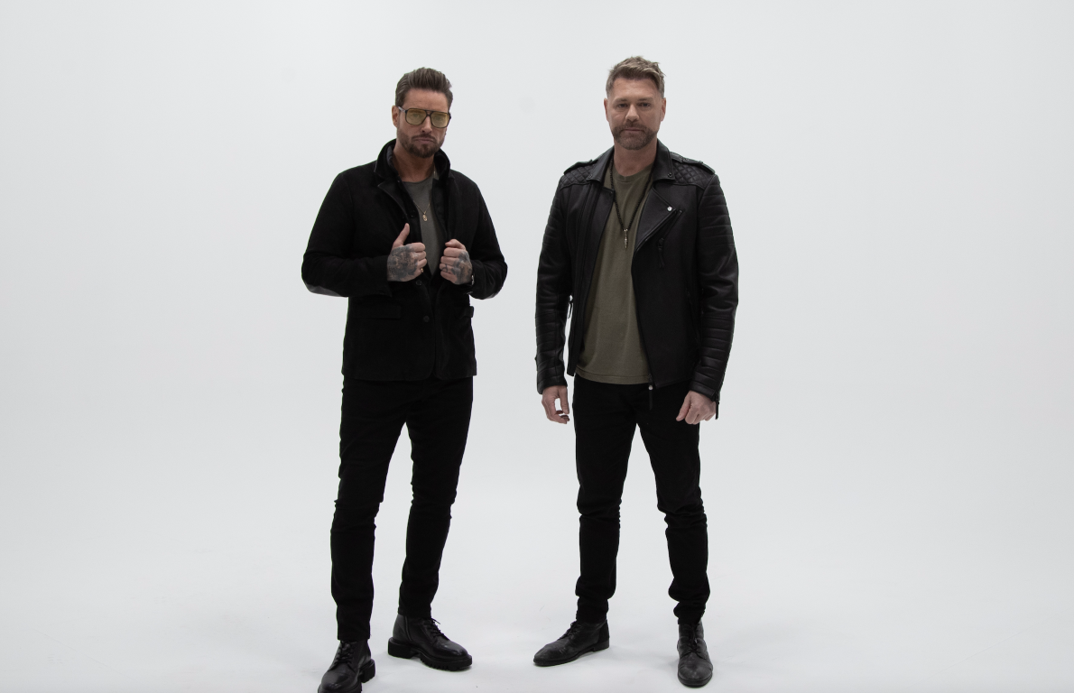Keith Duffy and Brian McFadden of Boyzlife standing side by side against a white studio background wearing black jackets and trousers