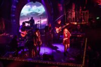 The Van Morrison Alumni Band performing live on stage with brass instruments and vocalists.