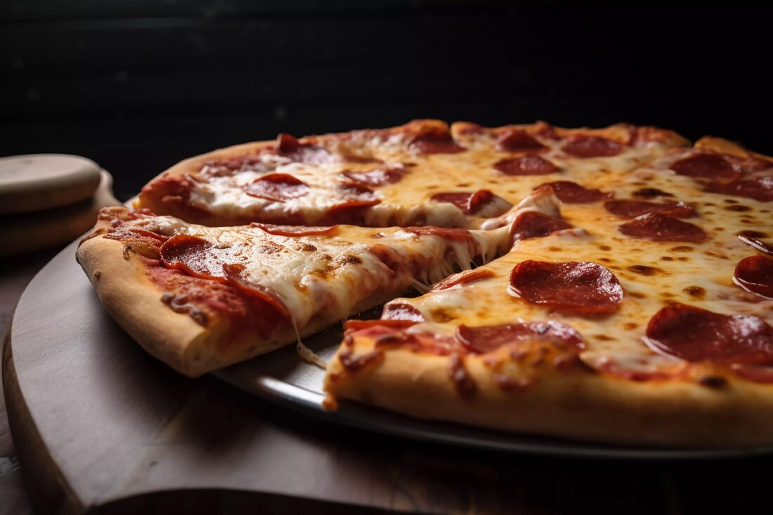 A freshly baked pepperoni pizza with melted cheese and a slice being pulled away, served on a round wooden board.