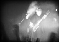 Atmospheric black and white photograph of bassist David J playing bass guitar on a smoky stage with Bauhaus